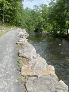 Trail walk way with a stone wall edge next to a stream of water. 