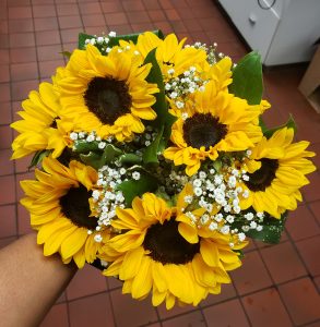 Close up of the top of a hand tied circular style bridal bouquet with sunflowers and baby's breath.