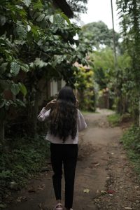 A girl walking through a path by speaking on the phone.The surrounding area is lush and green, suggesting a natural or garden setting.